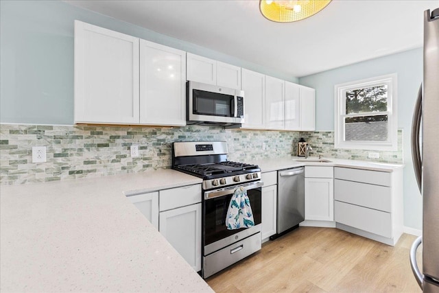 kitchen with stainless steel appliances, light wood finished floors, decorative backsplash, and white cabinetry