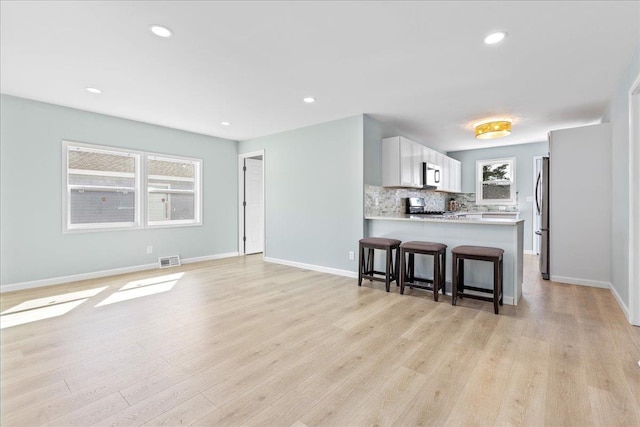 kitchen featuring visible vents, backsplash, a breakfast bar area, appliances with stainless steel finishes, and a peninsula