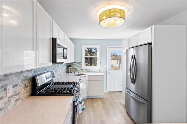 kitchen with tasteful backsplash, light wood-style flooring, appliances with stainless steel finishes, white cabinetry, and a sink