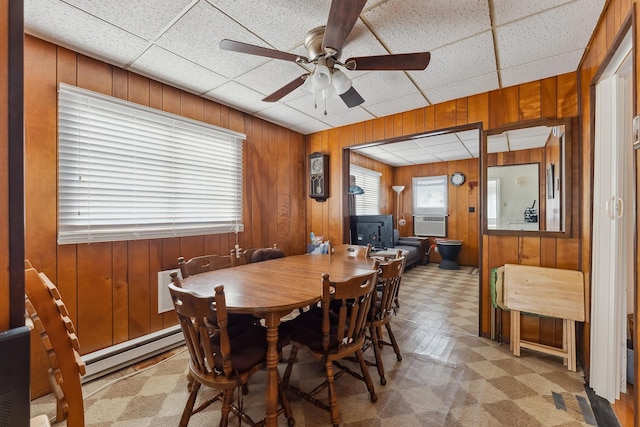 dining space featuring a baseboard heating unit, a paneled ceiling, wooden walls, and ceiling fan