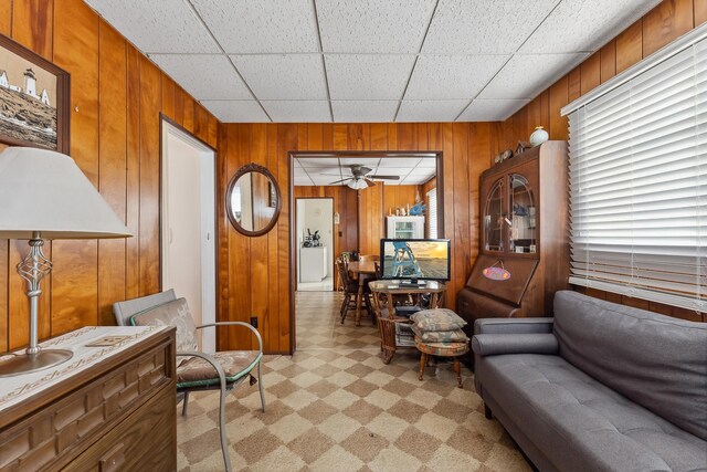 living area with light carpet, wood walls, a paneled ceiling, and ceiling fan