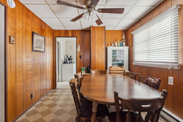 dining space featuring a drop ceiling, a baseboard heating unit, light floors, and wooden walls