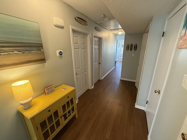 corridor with baseboards, a textured ceiling, wood finished floors, and attic access