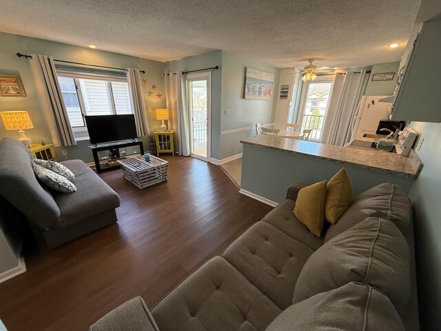 living area featuring a ceiling fan, dark wood-style flooring, baseboards, and a textured ceiling