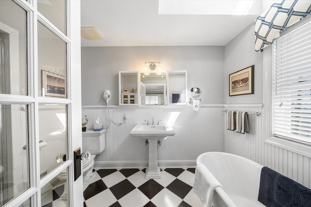 full bath with wainscoting, toilet, a freestanding tub, and tile patterned floors