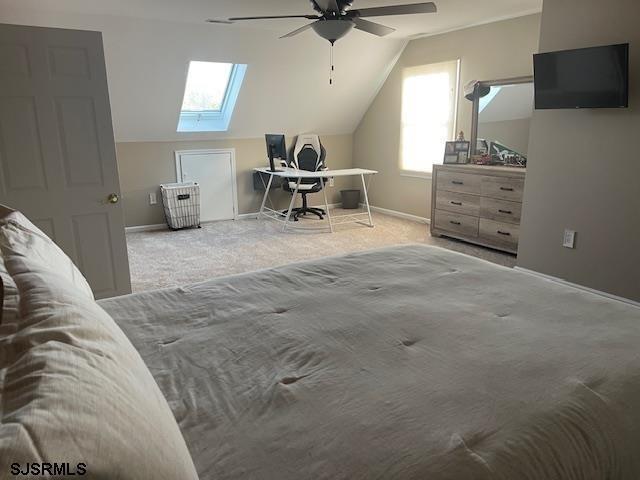 bedroom featuring light carpet, vaulted ceiling with skylight, and ceiling fan