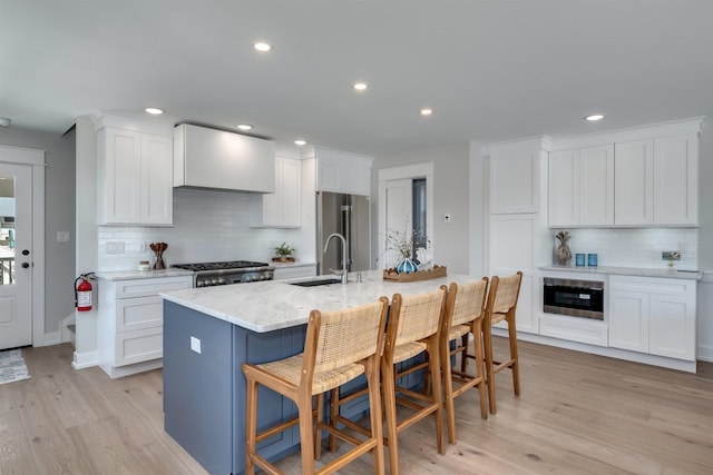 599 22nd St Unit 599, Avalon, NJ 08202 - kitchen with tasteful backsplash, stainless steel appliances, light wood-style flooring, wall chimney exhaust hood, and a kitchen breakfast bar