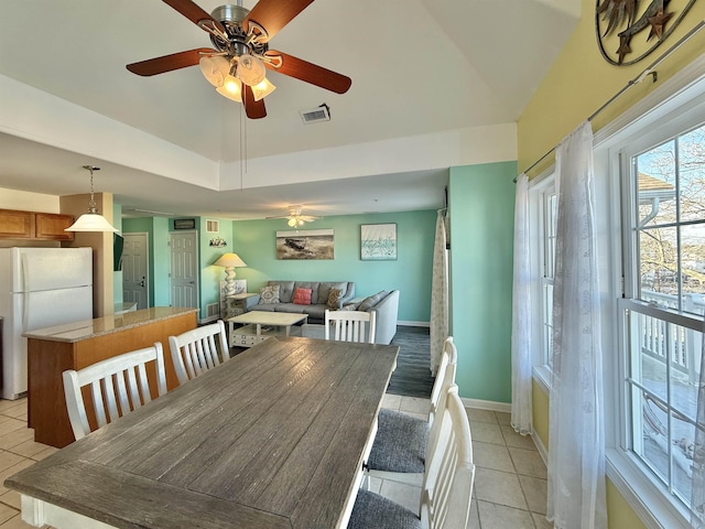 tiled dining area with ceiling fan and a tray ceiling