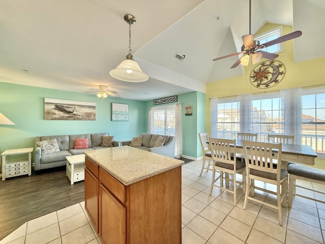 kitchen featuring pendant lighting, high vaulted ceiling, light tile patterned floors, ceiling fan, and light stone countertops