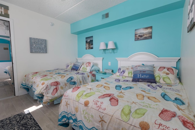 bedroom with wood tiled floor, a textured ceiling, and visible vents