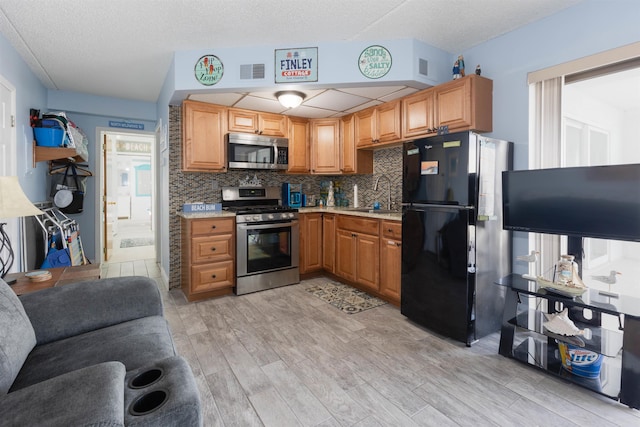 kitchen with a sink, light wood-type flooring, decorative backsplash, light countertops, and appliances with stainless steel finishes