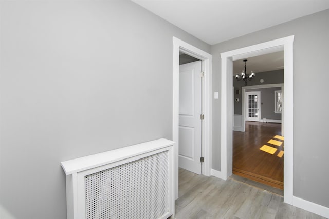 hall with radiator heating unit, baseboards, light wood-style floors, and an inviting chandelier