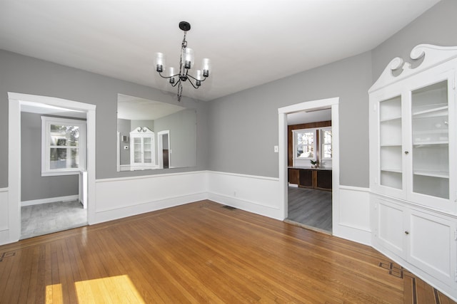 unfurnished dining area featuring visible vents, plenty of natural light, a notable chandelier, and hardwood / wood-style flooring