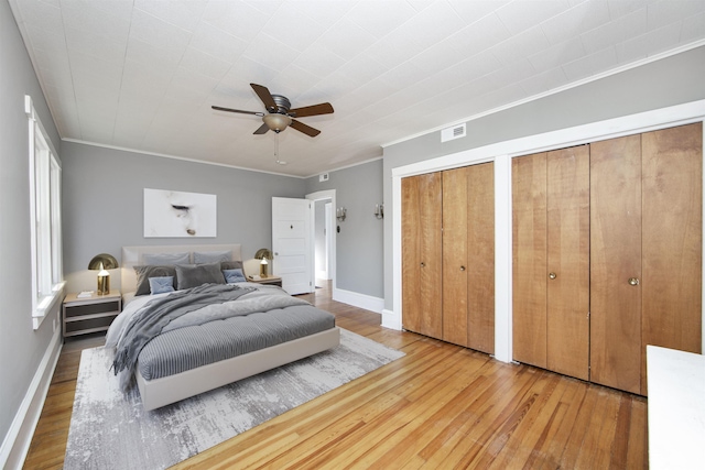 bedroom with visible vents, two closets, crown molding, baseboards, and wood finished floors