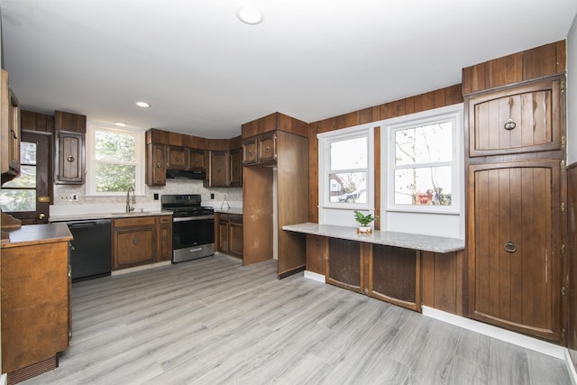 kitchen with light wood-style flooring, a sink, under cabinet range hood, black dishwasher, and stainless steel range with gas stovetop