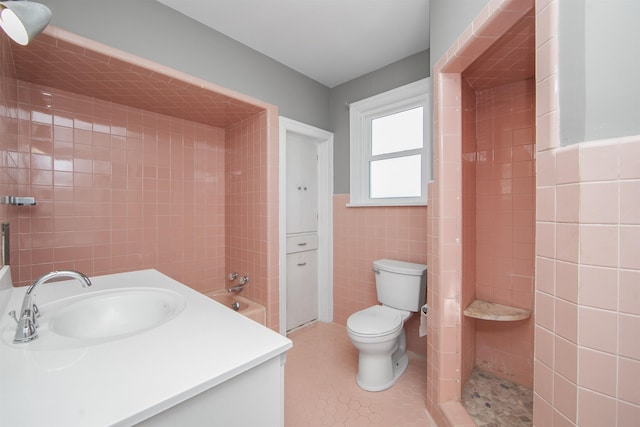 full bath with vanity, a wainscoted wall, tiled shower, tile walls, and toilet