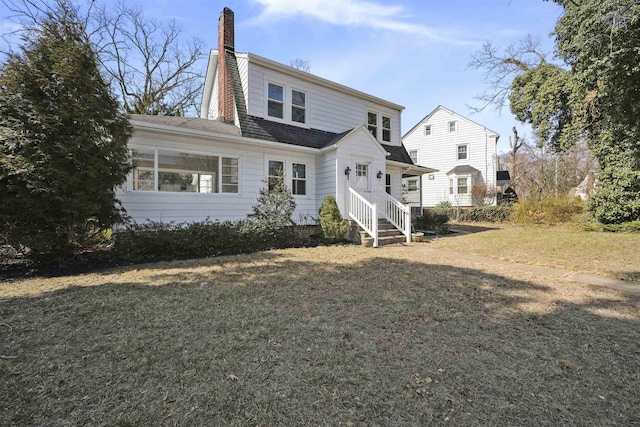 rear view of house with a yard, a chimney, and roof with shingles