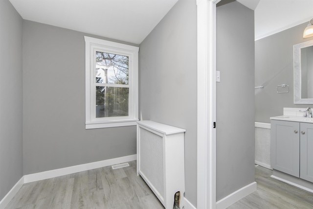 hall featuring a sink, baseboards, and light wood-style floors