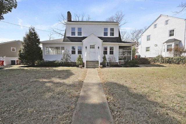 view of front of home with a shingled roof, a front lawn, a sunroom, and a chimney