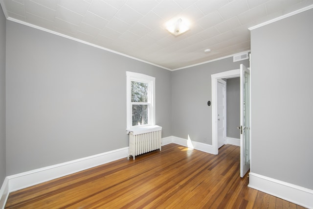 spare room with visible vents, baseboards, radiator heating unit, hardwood / wood-style floors, and ornamental molding