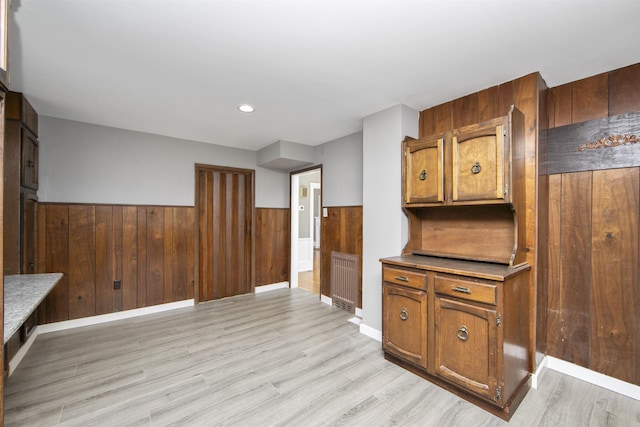 kitchen with a wainscoted wall, light wood-style floors, wood walls, and brown cabinetry