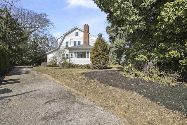 view of front of house featuring aphalt driveway, a gambrel roof, and a chimney