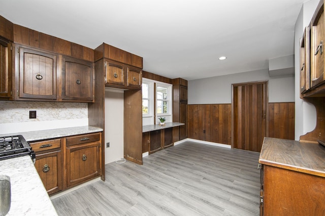 kitchen with light countertops, wood walls, wainscoting, light wood-type flooring, and backsplash