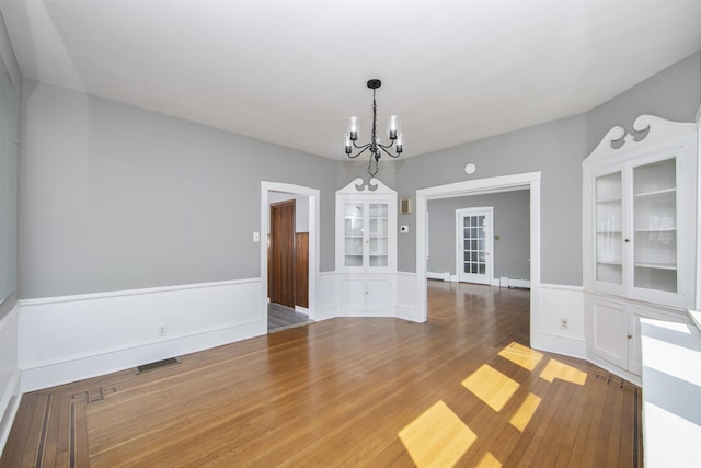unfurnished dining area featuring visible vents, a wainscoted wall, a notable chandelier, and wood finished floors