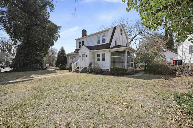 view of front of house featuring a gambrel roof, a sunroom, a shingled roof, a chimney, and a front lawn