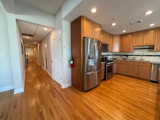 kitchen featuring appliances with stainless steel finishes, backsplash, light wood-type flooring, light stone countertops, and sink