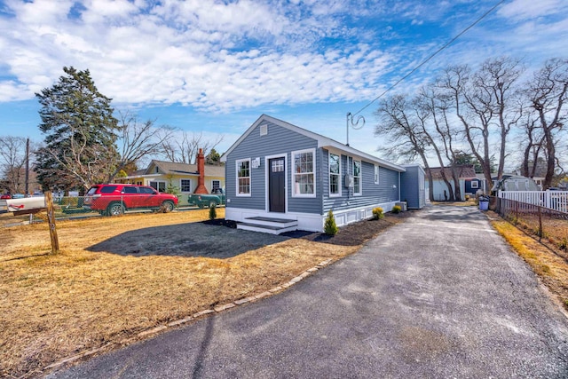 view of front of home featuring a front yard, fence, aphalt driveway, and an outbuilding