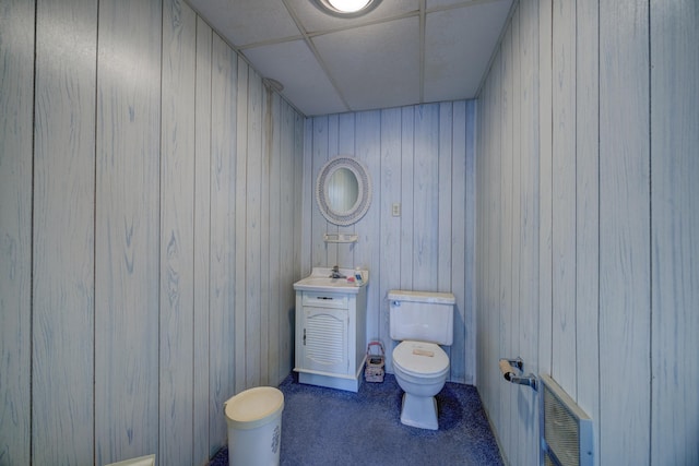 bathroom featuring sink, toilet, a paneled ceiling, and wood walls