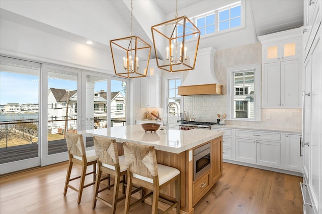 kitchen featuring white cabinetry, stainless steel microwave, a center island with sink, and pendant lighting