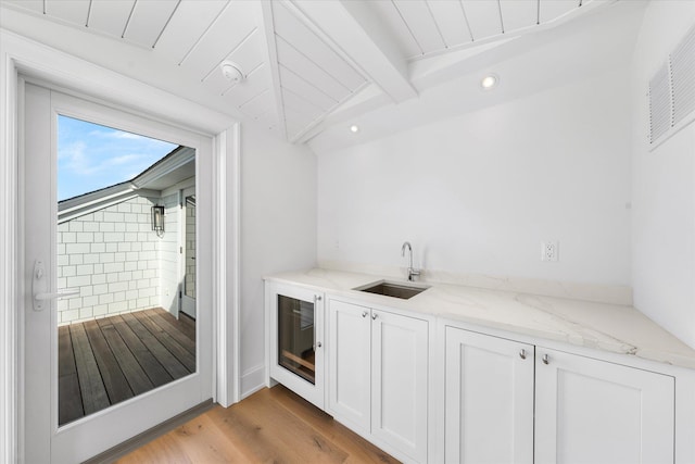 bar featuring light stone counters, sink, lofted ceiling with beams, and white cabinets