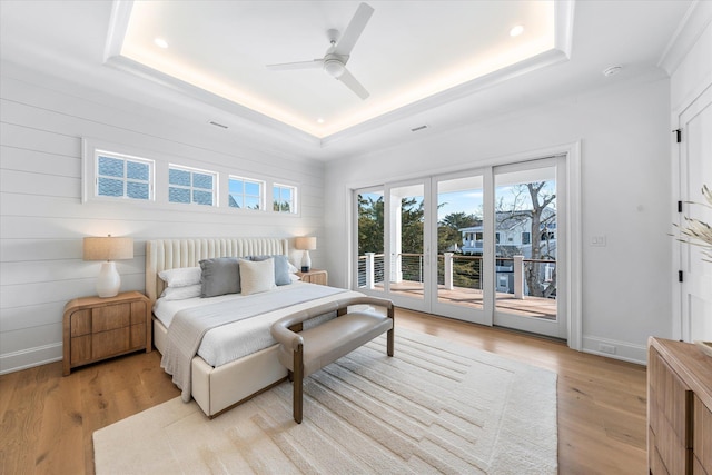 bedroom with ceiling fan, access to exterior, light wood-type flooring, and a tray ceiling