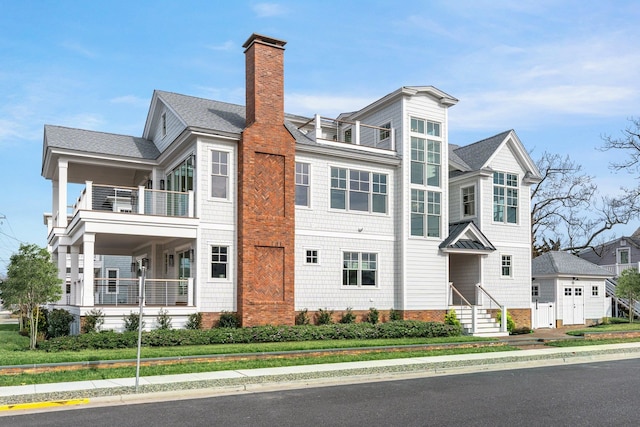 view of front of home featuring a shingled roof, a chimney, and a balcony