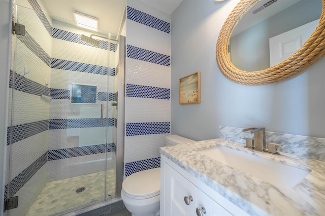 full bathroom featuring toilet, vanity, a shower stall, and visible vents