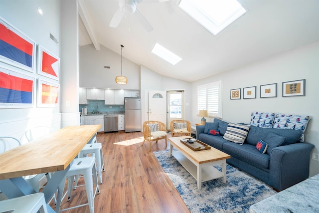 living area featuring a skylight, light wood finished floors, visible vents, a ceiling fan, and high vaulted ceiling