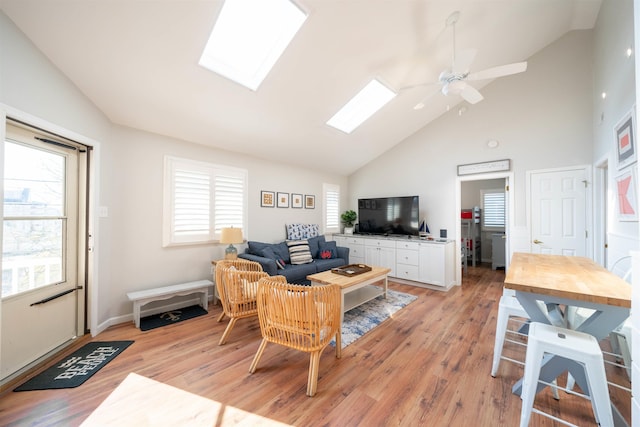 living area with ceiling fan, high vaulted ceiling, a skylight, and light wood-style floors