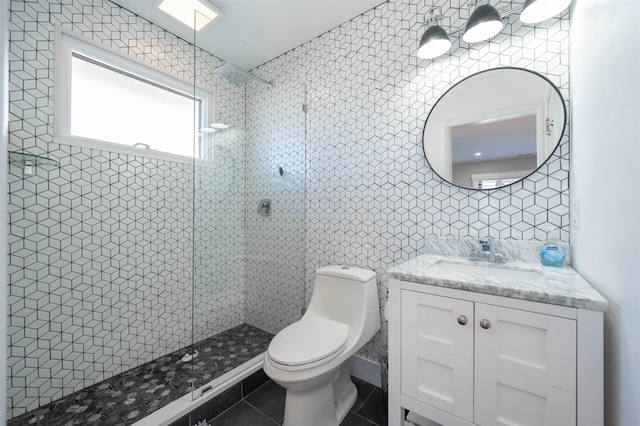 bathroom with toilet, tile patterned flooring, a tile shower, vanity, and tile walls