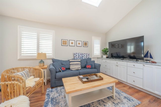 living area with vaulted ceiling with skylight and light wood-style flooring