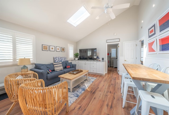 living area with light wood-style floors, a skylight, ceiling fan, and high vaulted ceiling