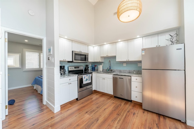 kitchen with stainless steel appliances, a towering ceiling, light wood-style floors, white cabinets, and a sink