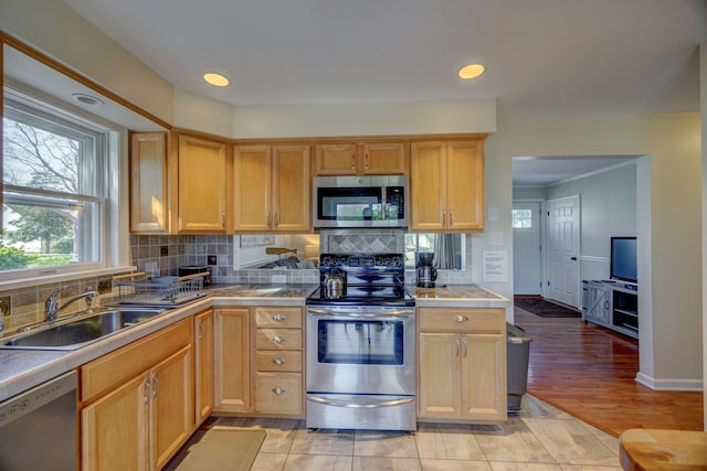kitchen featuring stainless steel appliances, light brown cabinetry, a sink, decorative backsplash, and tile counters