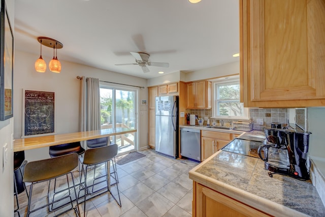 kitchen featuring stainless steel appliances, light brown cabinetry, decorative backsplash, a ceiling fan, and tile countertops