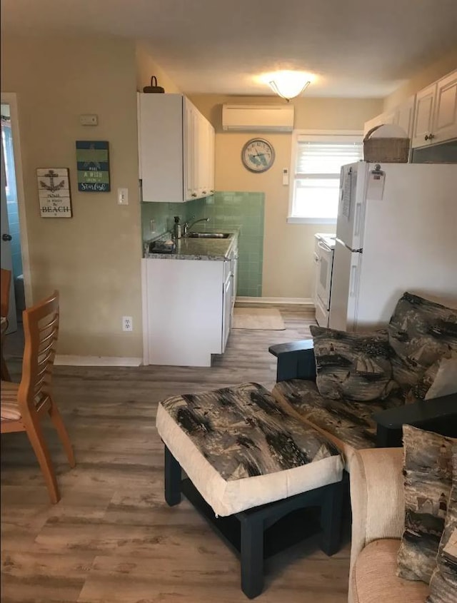 kitchen with sink, white appliances, light hardwood / wood-style flooring, a wall mounted air conditioner, and white cabinets