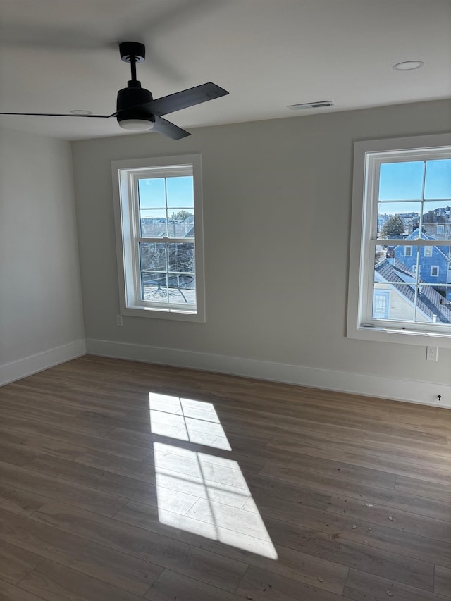 empty room featuring dark wood-type flooring, ceiling fan, and a wealth of natural light