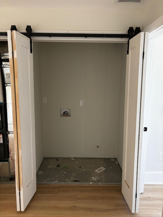 washroom with a barn door, washer hookup, and light hardwood / wood-style floors