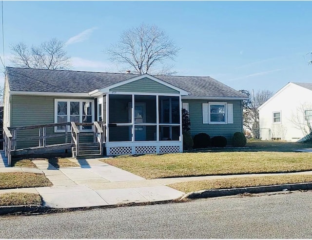 view of front of house featuring a front yard, a sunroom, and a shingled roof