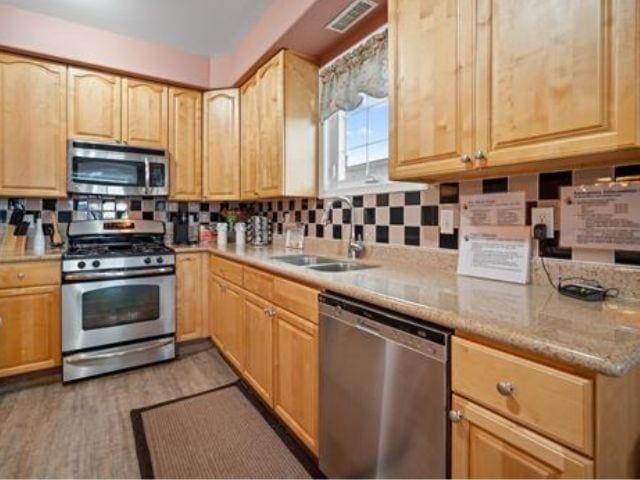 kitchen with tasteful backsplash, light stone countertops, appliances with stainless steel finishes, and sink